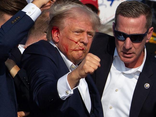 US Republican candidate Donald Trump is seen with blood on his face surrounded by secret service agents as he is taken off the stage at a campaign event at Butler Farm Show Inc. in Butler, Pennsylvania, on July 13, 2024. Trump was hit in the ear in an apparent assassination attempt by a gunman at a campaign rally on Saturday, in a chaotic and shocking incident that will fuel fears of instability ahead of the 2024 US presidential election. The 78-year-old former president was rushed off stage with blood smeared across his face after the shooting in Butler, Pennsylvania, while the gunman and a bystander were killed and two spectators critically injured. (Photo by Rebecca DROKE / AFP) / QUALITY REPEAT