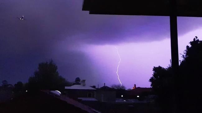 A plane flies over amid a lightning storm, as seen from North Adelaide. Picture: Kate Jarmyn