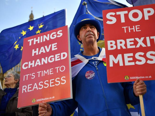 (FILES) In this file photo taken on November 14, 2018 Pro-European Union (EU), anti-Brexit demonstrator Steve Bray holds placards and wave Union and EU flags as they protest outside of the Houses of Parliament in London. - A single voice rings out through the ornate corridors of the Houses of Parliament, a regular shout from the street with a simple message: "Stoooppp Brexit!" Wearing a blue top hat with a gold band styled on the European Union flag, Steve Bray has spent more than a year honing his voice in an extraordinarily persistent protest. (Photo by Ben STANSALL / AFP)