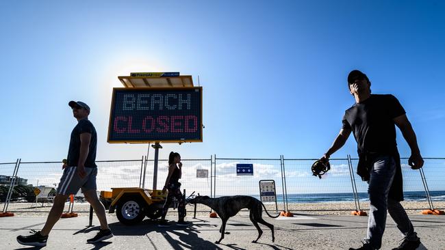 People walking on the promenade near a BEACH CLOSED sign at Sydney’s Bronte Beach.