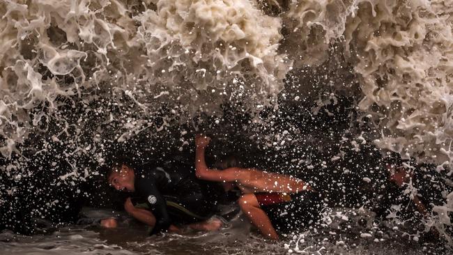 TOPSHOT – Young men crouch behind a wall as they play in record-breaking waves caused by the outer fringe of Tropical Cyclone Alfred at Point Danger in Coolangatta on March 7, 2025. Violent winds toppled power lines on March 7 as Tropical Cyclone Alfred inched towards Australia's eastern coast, sparking evacuation orders and leaving more than 50,000 homes without electricity. (Photo by DAVID GRAY / AFP)