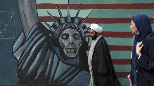 A cleric and a woman walk past an anti-US mural painted on the wall of the former US embassy in Tehran. Picture: AP