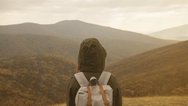 Hiker woman with backpack enjoying landscape of autumn mountains, rear view