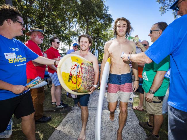 Surfers Liam Egan and Dave Lauchs work their way through a sea of Party volunteers to vote in the State of Election after enjoying most of the day in the water at Alexandra Headland. Picture: Lachie Millard