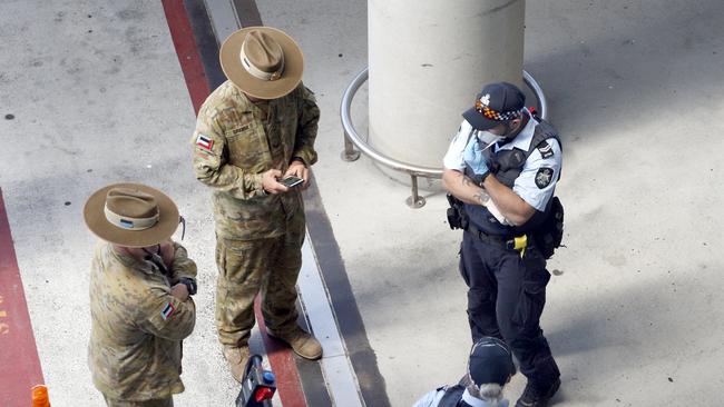 Police and Army personnel watch as passengers arrive into Brisbane International Airport Picture: Steve Pohlner