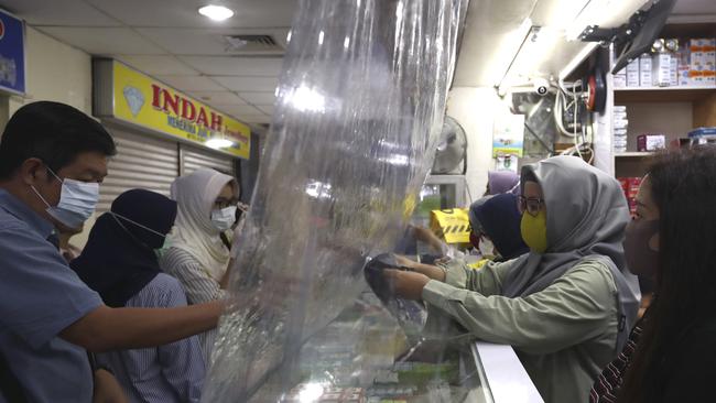 Shop attendants serve customers behind a sheet of plastic installed to help curb the spread of the coronavirus at a pharmacy in Jakarta. Picture: AP