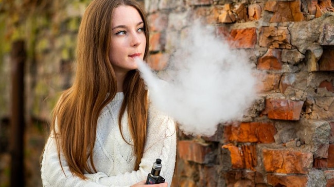 Vaping teenager. Young pretty white caucasian teenage girl with problem skin smoking an electronic cigarette the ruined brick wall on the street in the autumn. Bad habit. Vape activity.