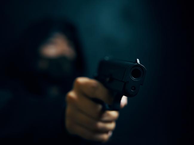 Man in hood threatens with firearm. Masked robber with gun. Weapon in person's hands. Murderer or armed thief. Criminal with pistol. Generic image. Picture: Savusia Konstantin