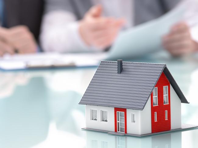 Businessman signs contract behind home architectural model. Image: iStock