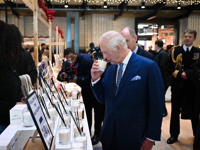 Charles sniffs a candle as he meets with traders during a visit to the Christmas market at the old Battersea Power Station. Picture: AFP