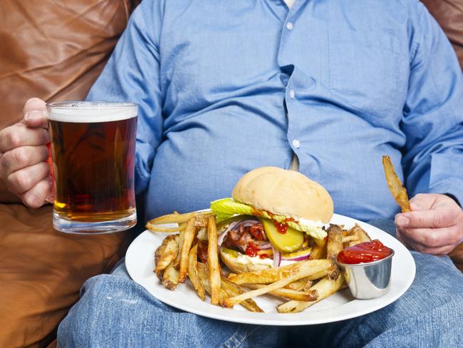 A photo of an overweight man sitting on an old couch with a very large unhealthy meal on his lap and a pint of beer in his hand. Obesity is a major cause of diabetes.