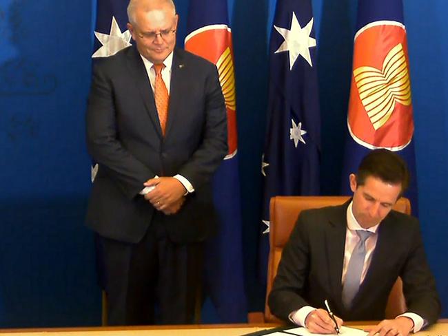 Trade Minister Simon Birmingham signs the Regional Comprehensive Economic Partnership on Sunday, as Prime Minister Scott Morrison looks on. Picture: AFP/ Vietnam Host Broadcaster