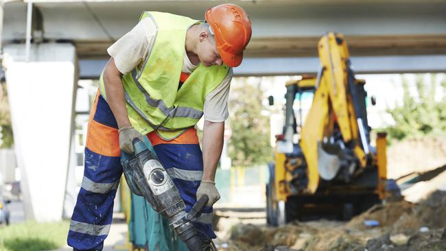 Builder worker with pneumatic hammer drill equipment breaking asphalt at road construction site