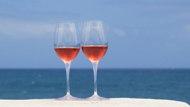 two glasses of rose wine on a whitewashed wall, blue ocean in the background