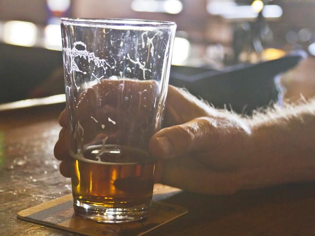 Close up of a man's hand grasping a mostly drunk, glass of beer with trails of suds on a bar coaster