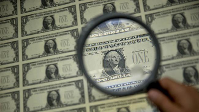 A person uses a magnifying glass to examine US dollar bills. Picture: Bloomberg