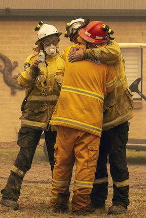 Bawley Point RFS captain John Sharpe (red helmet) was overcome with emotion as his colleagues helped him extinguish a blaze surrounding his home in Bawley Point, on the NSW south coast. Picture: Gary Ramage