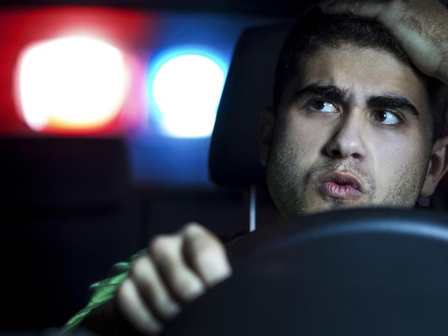 Police in pursuit of a reckless driver at night. About 30 years old Caucasian man, worried and holding his head, looking back at a police car. Police Melbourne drivers istock