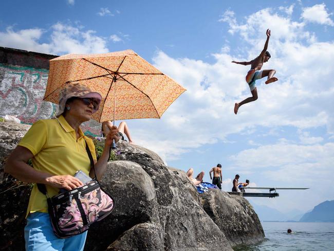 A boy jumps into Geneva Lake in Saint Saphorin, western Switzerland, above a tourist protecting herself from the sun with an umbrella. Picture: Fabrice Coffrini