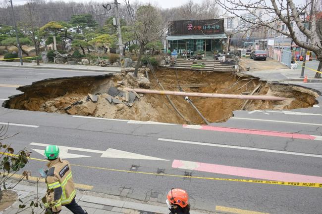Rescue workers walk past a sinkhole outside a plant shop on a road in Seoul