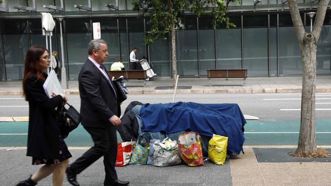 Pedestrians walk past a homeless man sleeping on a bench in Brisbane. Picture: NCA NewsWire/Tertius Pickard