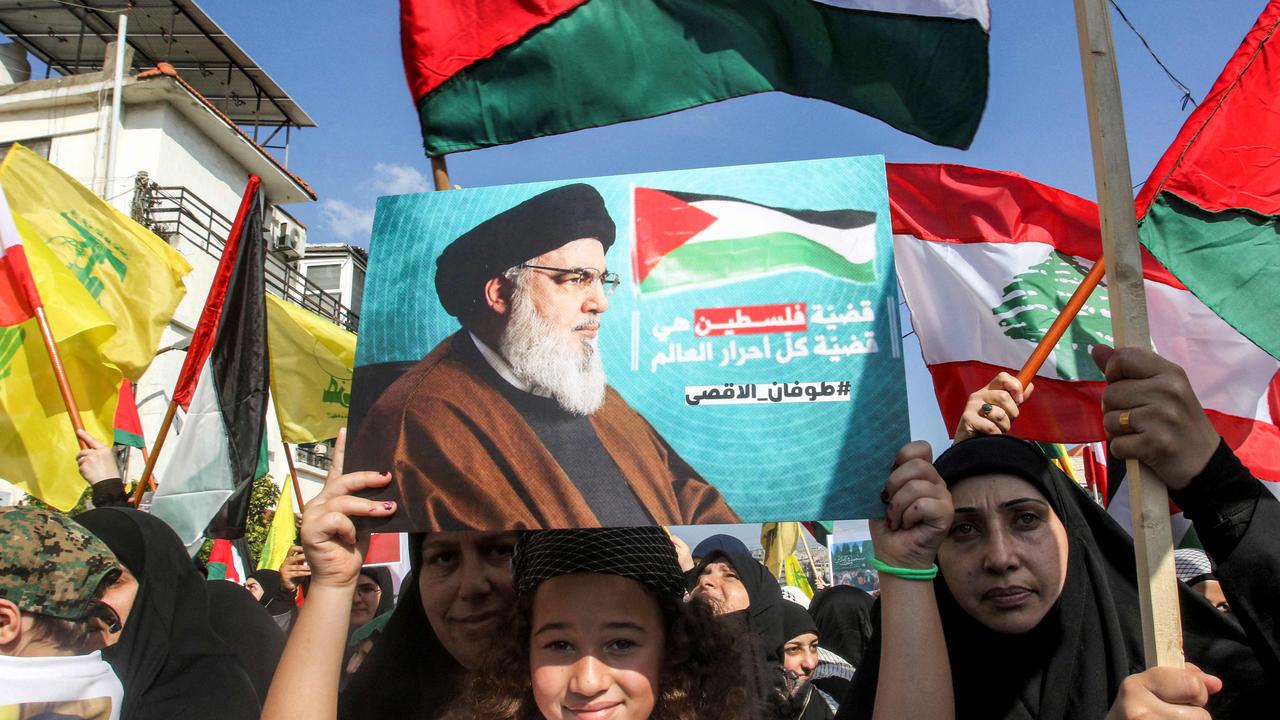 A girl holds up a sign showing Hassan Nasrallah, the leader of Lebanese Shiite movement Hezbollah, while others around her wave Palestinian, Lebanese, and Hezbollah flags. Picture: AFP