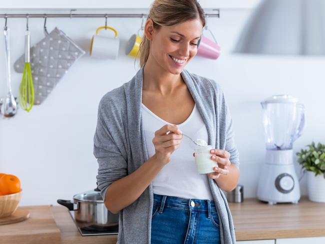 Shot of pretty young woman eating yogurt while standing in the kitchen at home.