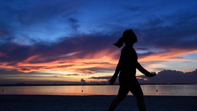 A woman walks along Brighton-Le-Sands Beach as the sun rises over Botany Bay. (AAP Image/Dean Lewins)