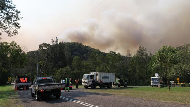 The Three Mile fire burns behind a ridge as Wisemans Ferry Rd is closed at Mill Creek, west of Gunderman. Picture: Richard Noone