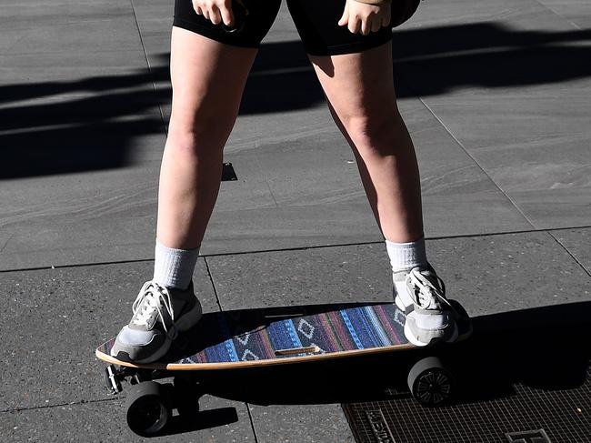 BRISBANE, AUSTRALIA - NewsWire Photos - JULY 7, 2021.A masked motorised skateboard rider waits for the light to change as she commutes through central Brisbane during the morning rush hour. Queensland's recent lockdown has ended but some restrictions, including wearing masks in public, remain.Picture: NCA NewsWire / Dan Peled