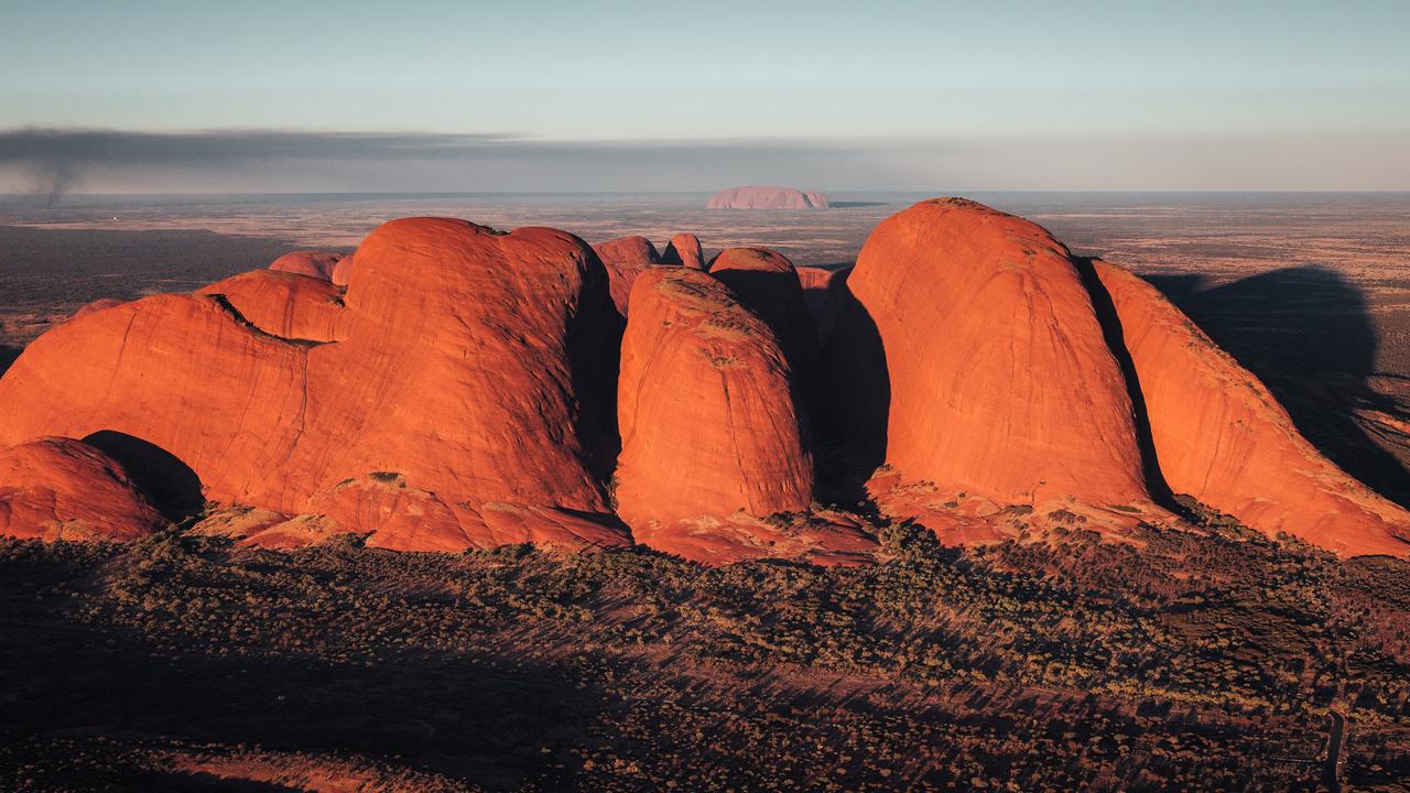 Aerial view of Kata Tjuta at sunrise with Uluru seen in the background. Picture: Colby Brown/Tourism NT