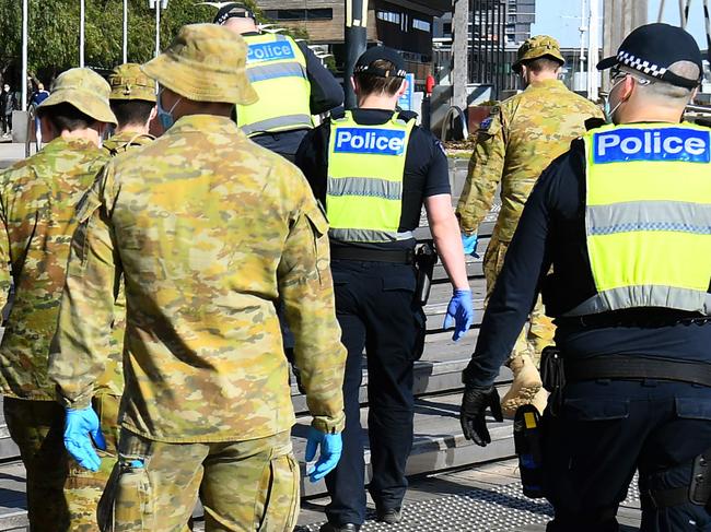 A man waves to a group of police and soldiers patrolling the Docklands area of Melbourne on August 2, 2020, after the announcement of new restrictions to curb the spread of the COVID-19 coronavirus. - Australia on August 2 introduced sweeping new measures to control a growing coronavirus outbreak in its second-biggest city, including an overnight curfew and a ban on weddings for the first time during the pandemic. (Photo by William WEST / AFP)