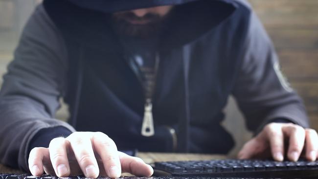 hacker in the black hood in a room with wooden walls makes cybercrime istock image