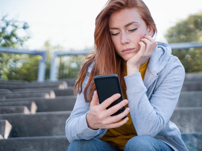 Worried young woman holding mobile phone waiting message