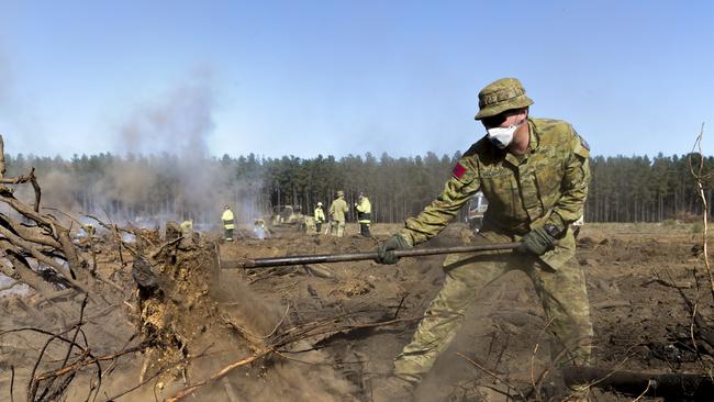 Australian Army Gunner Malachy Brandwood from the 9th Regiment, Royal Australian Artillery rakes burning wood to assist the Country Fire Service in putting out hot spots to prevent reignition of bushfires on Kangaroo Island during Operation Bushfire Assist 2019-2020.