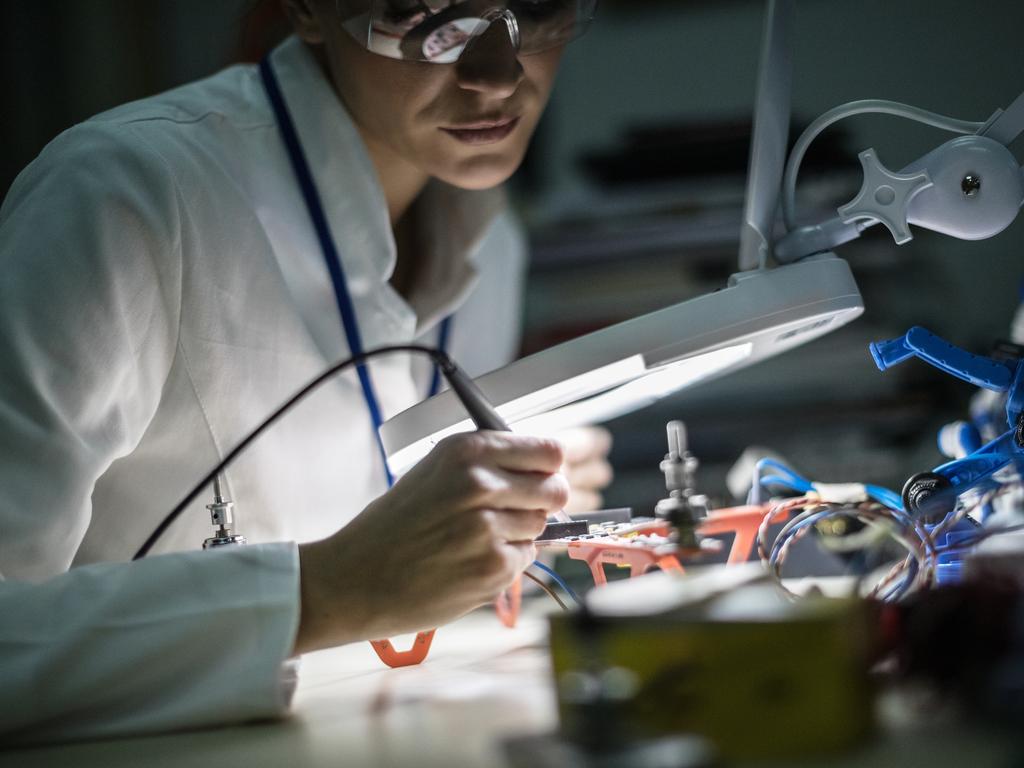 ELECTRONIC/ ENGINEERING CAREERS FOR WOMEN:  Mid adult female electrician working on drone at desk in industry, using magnifying glass;  Robotics generic