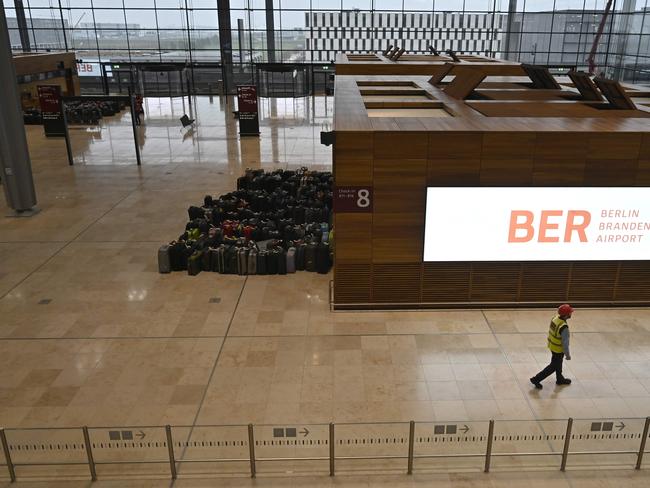 A man walks past suitcases to test the baggage carousel are piled at a check-in counter inside the entry hall to the Berlin-Brandenburg Willy-Brandt international Airport in Schoenefeld, near Berlin, on November 25, 2019. (Photo by Tobias SCHWARZ / AFP)