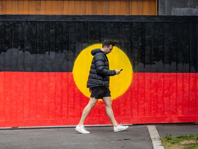 VOICEREF23. A Pedestrian walks past a gate painted in the Aboriginal flag on the day of the referendum in South Yarra, VIC. Melbourne. Picture: Jake Nowakowski