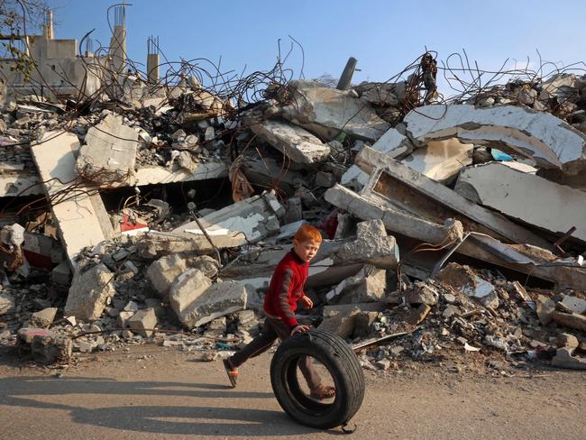 A boy plays with a rubber tyre next to the rubble of buildings destroyed in Israeli airstrike near the Nuseirat refugee camp in the central Gaza Strip on January 11, 2025, as the war between Israel and Hamas militants continues. (Photo by Eyad BABA / AFP)