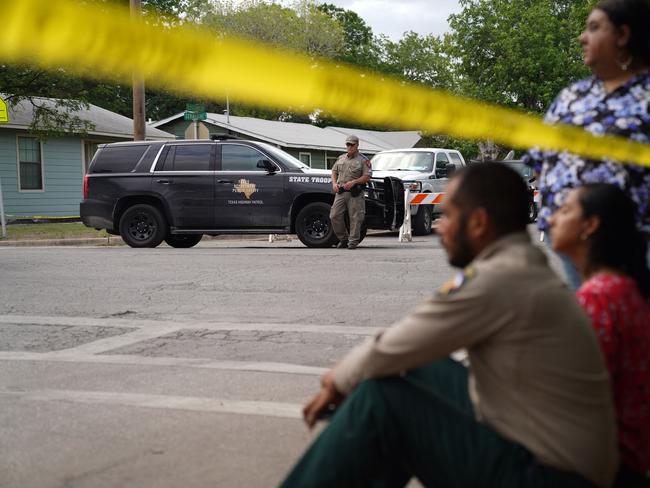 People sit on the curb outside of Robb Elementary School as State troopers guard the area in Uvalde, Texas.