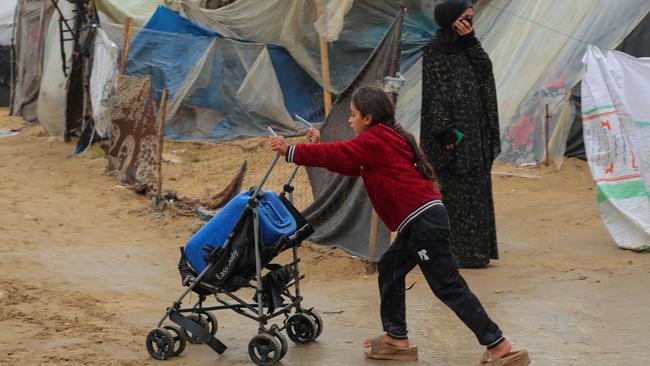 A girl uses a baby stroller to ferry drinking water in rainy weather at a makeshift tent camp in Rafah. Picture: Mohammed Abed/AFP