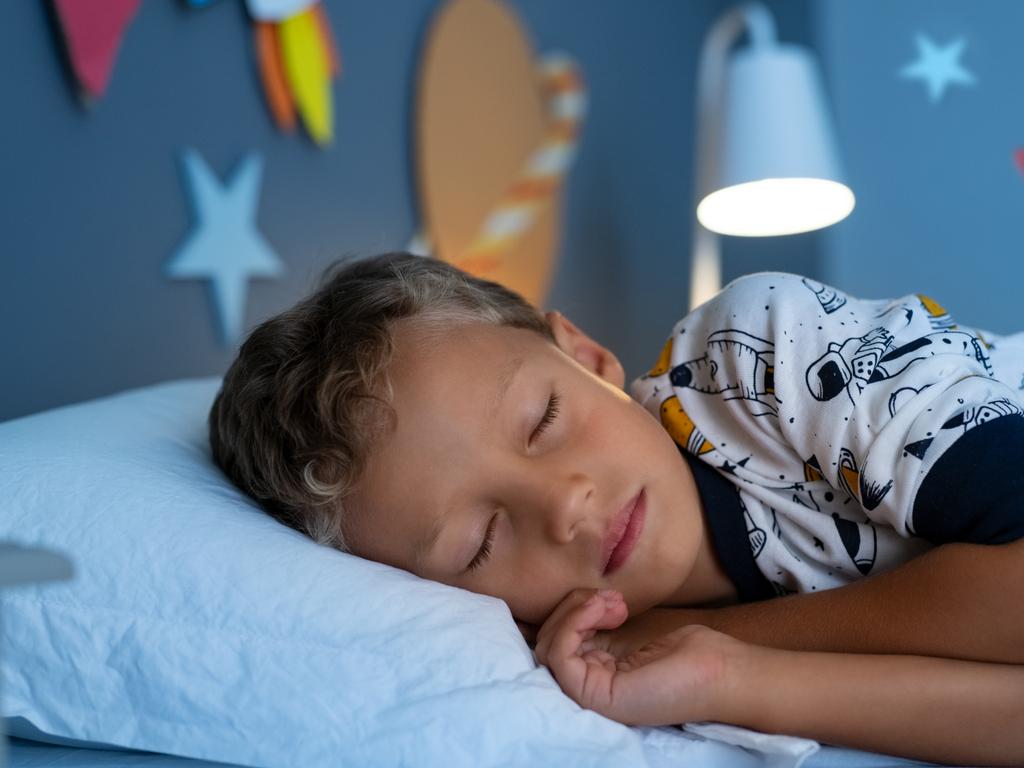 Cute little boy lying on side on bed and sleeping in bedroom decorated with planets and stars. Child sleeping in decorated room and dreams of going into space. Kid sleeps deeply with closed eyes in his space themed room and dreaming of being an astronaut.