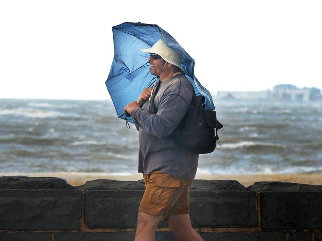 A man shields himself from the heavy rain and strong winds as he walks along Beaconsfield Parade at Middle Park. Picture: Andrew Henshaw