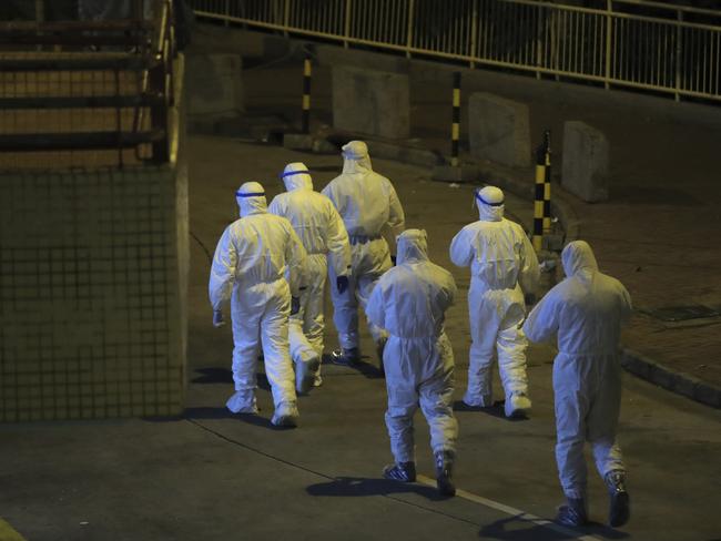 People wearing protective suits walk by an entrance at the Cheung Hong Estate, a public housing estate, during evacuation of residents in Hong Kong, Tuesday, Feb. 11, 2020. The Centre for Health Protection of the Department of Health evacuated some residents from the public housing estate after a few cases of novel coronavirus infection to stop the potential risk of further spread of the virus. (AP Photo/Kin Cheung)