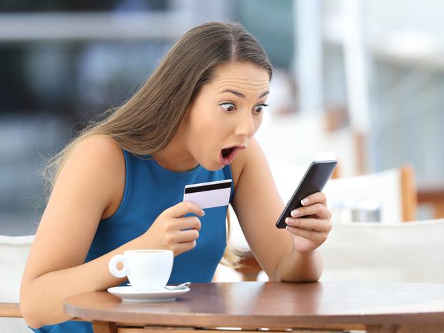 Single astonished buyer holding phone and credit card finding a good offer on line sitting in a restaurant Picture: iStock.