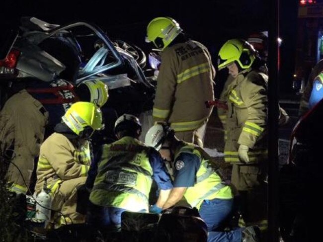 Emergency services and paramedics tend to Josh at the crash scene. The twisted wreck of the car can be seen in the background.