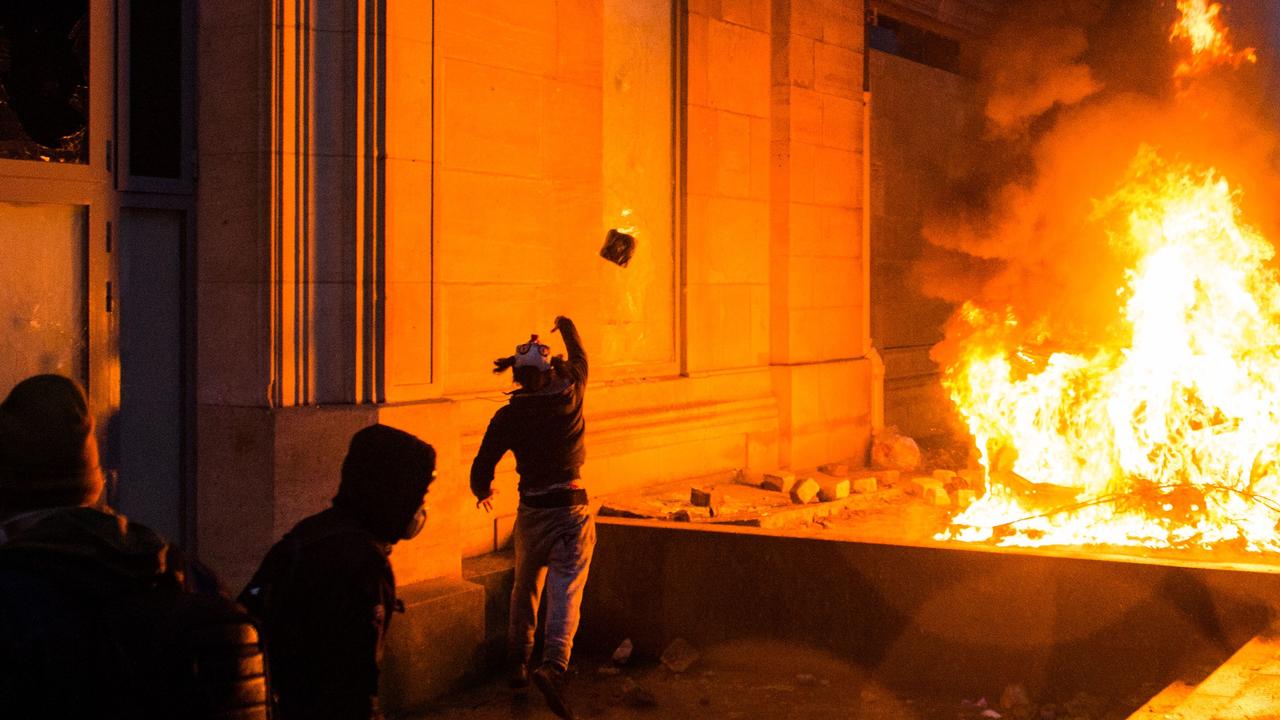 A man throws a stone next to the broken windows of the Musee de l'Orangerie (L) and a burning vehicle (R), on the Tuileries Garden, during a protest of Yellow vests. Picture: AFP