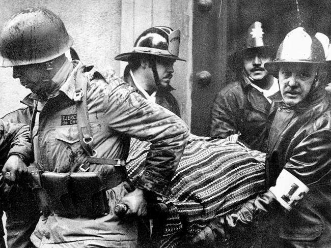 Soldiers and firefighters carry the body of Chile’s President Salvador Allende, wrapped in a Bolivian poncho, out the destroyed presidential palace of La Moneda after coup. Picture: AP