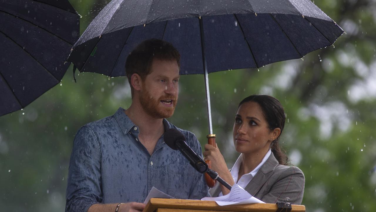 Prince Harry’s wife Meghan holds an umbrella over him as he addresses the public during a community event in Dubbo on October 17. Picture: Ian Vogler/Getty Images