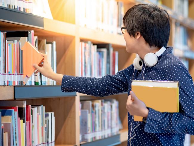 Generic image of a man picking books from a shelf at a library.